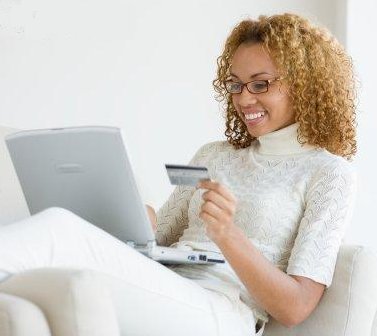 Woman using a laptop and holding a credit card, smiling.