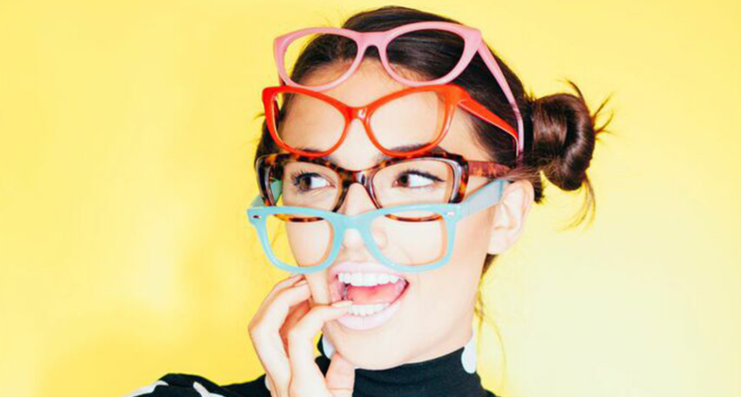 Person wearing multiple pairs of glasses in different colors: pink, red, tortoiseshell, and blue.