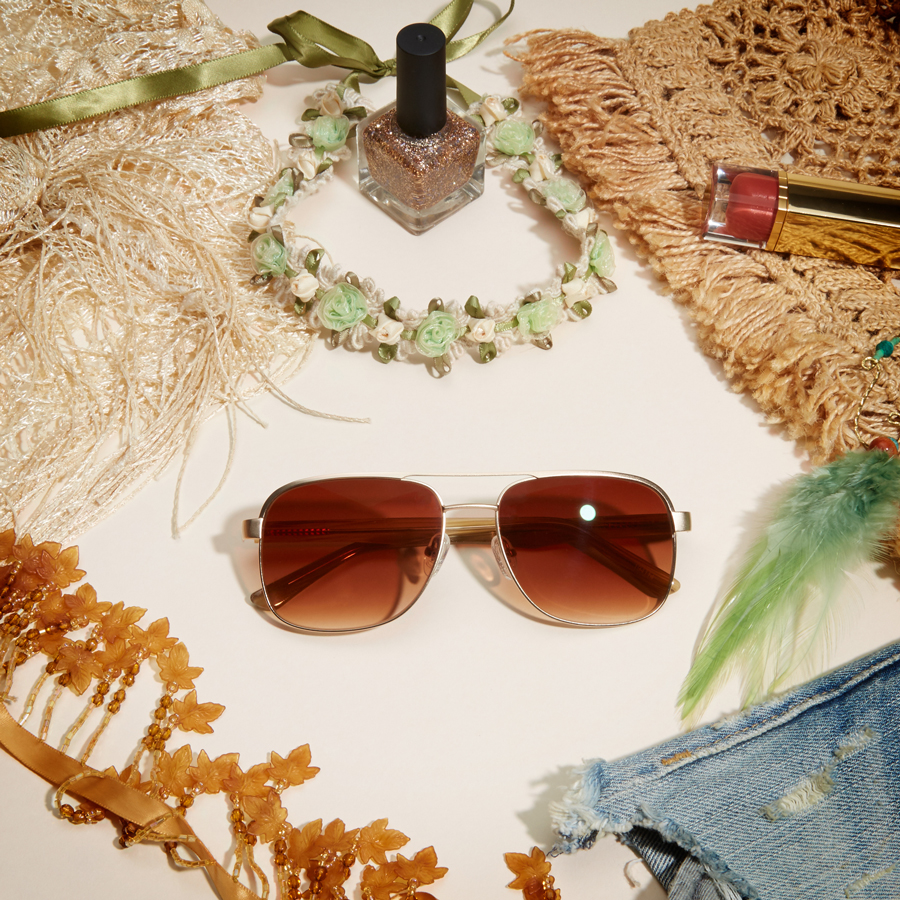 Gold-framed sunglasses with brown-tinted lenses, amidst assorted accessories.