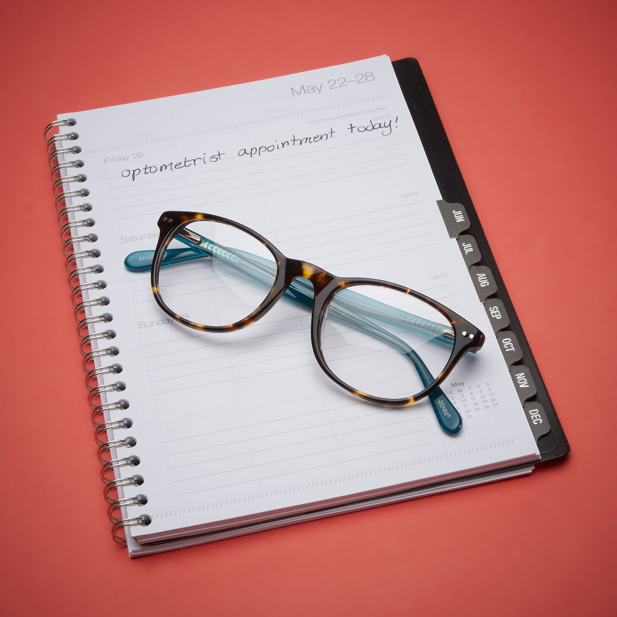 Eyeglasses resting on an open planner. Text in planner: May 22-28, Optometrist appointment today!