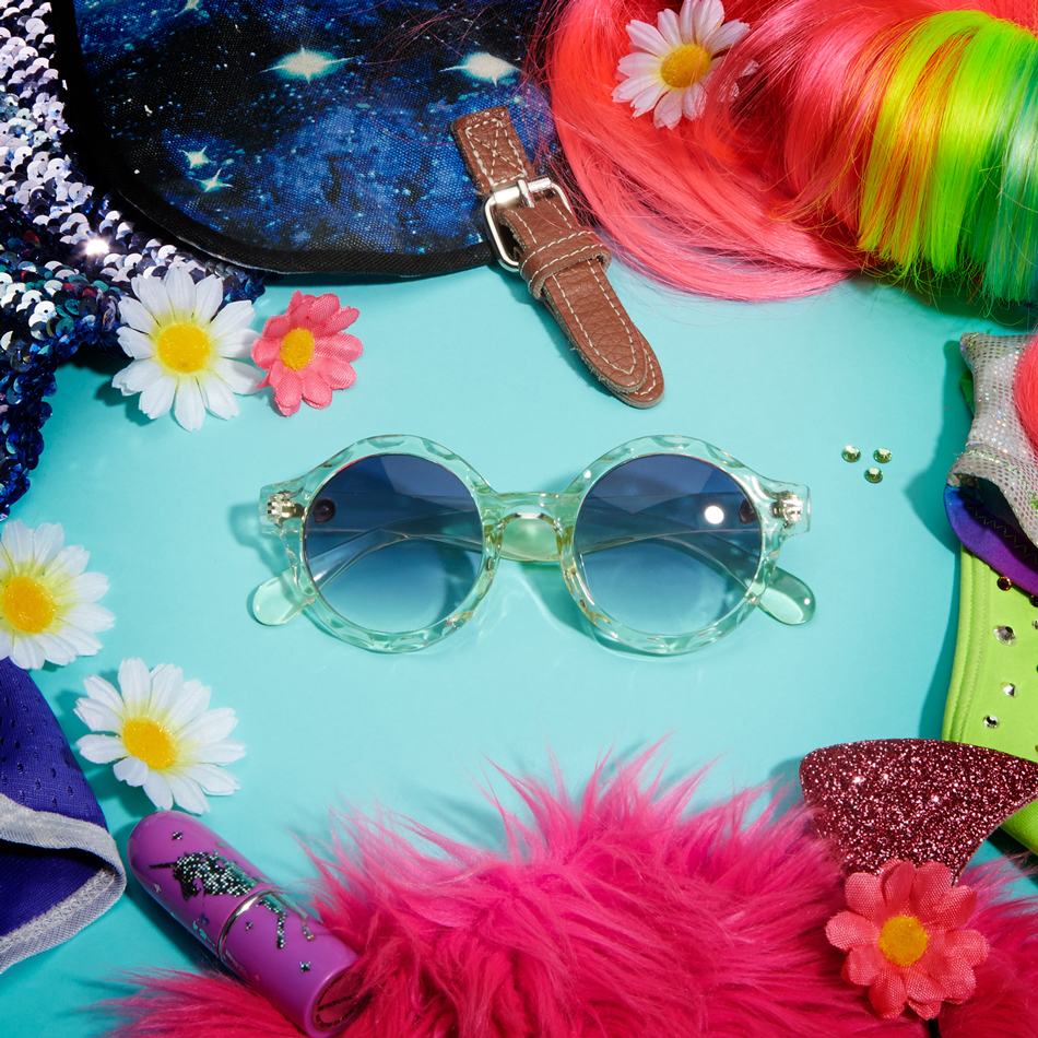Round sunglasses with clear frames and blue lenses surrounded by colorful flowers and sequined accessories.