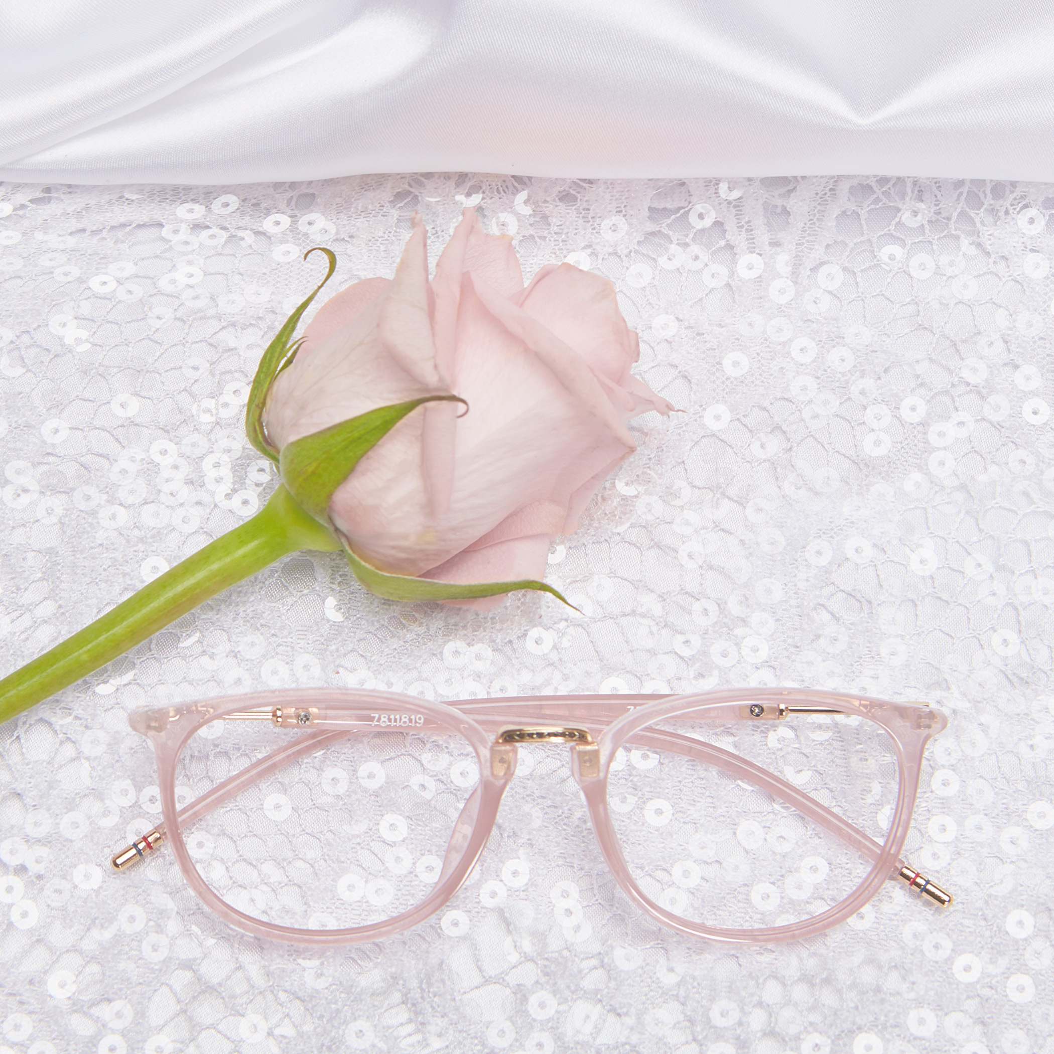 Pink eyeglasses with the text "7811819" on lace fabric, next to a pink rose.