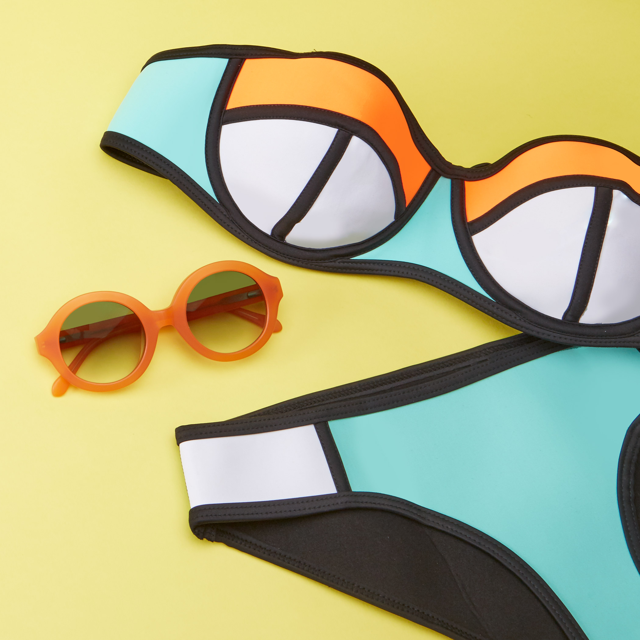 Color-block bikini with turquoise, orange, white, and black patterns, paired with orange round sunglasses.