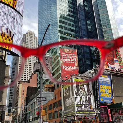 Red Oakley glasses frame a busy city street with tall buildings and colorful billboards.