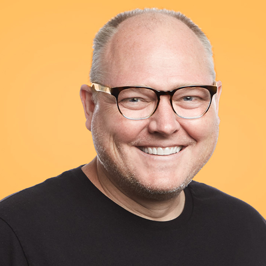 Man wearing black-framed glasses and smiling, orange background.