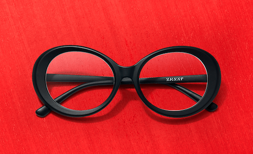 Black oval eyeglasses with "Warby" inscribed on the inner right arm, displayed on a red background.