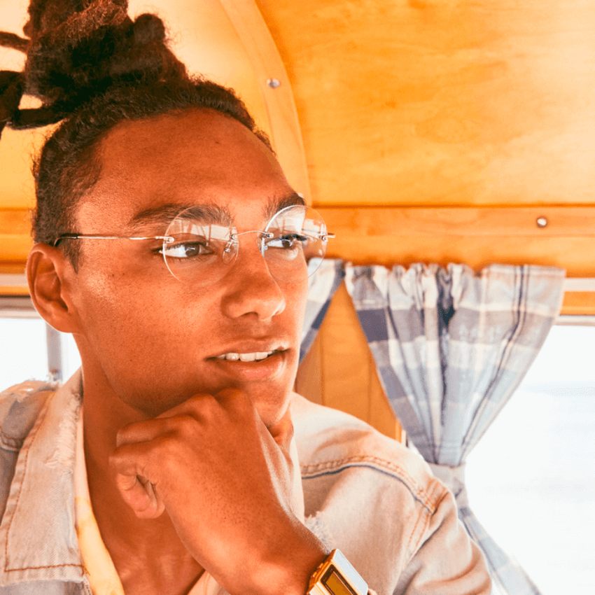 Person wearing transparent round glasses and a gold digital watch, resting their chin on their hand.