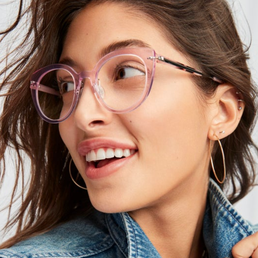 Woman wearing clear pink round eyeglasses and a denim jacket.