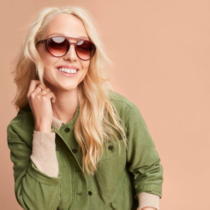Blonde woman wearing large, round, gradient sunglasses and a green jacket.