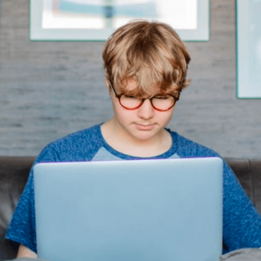 Teenager wearing glasses using a laptop.