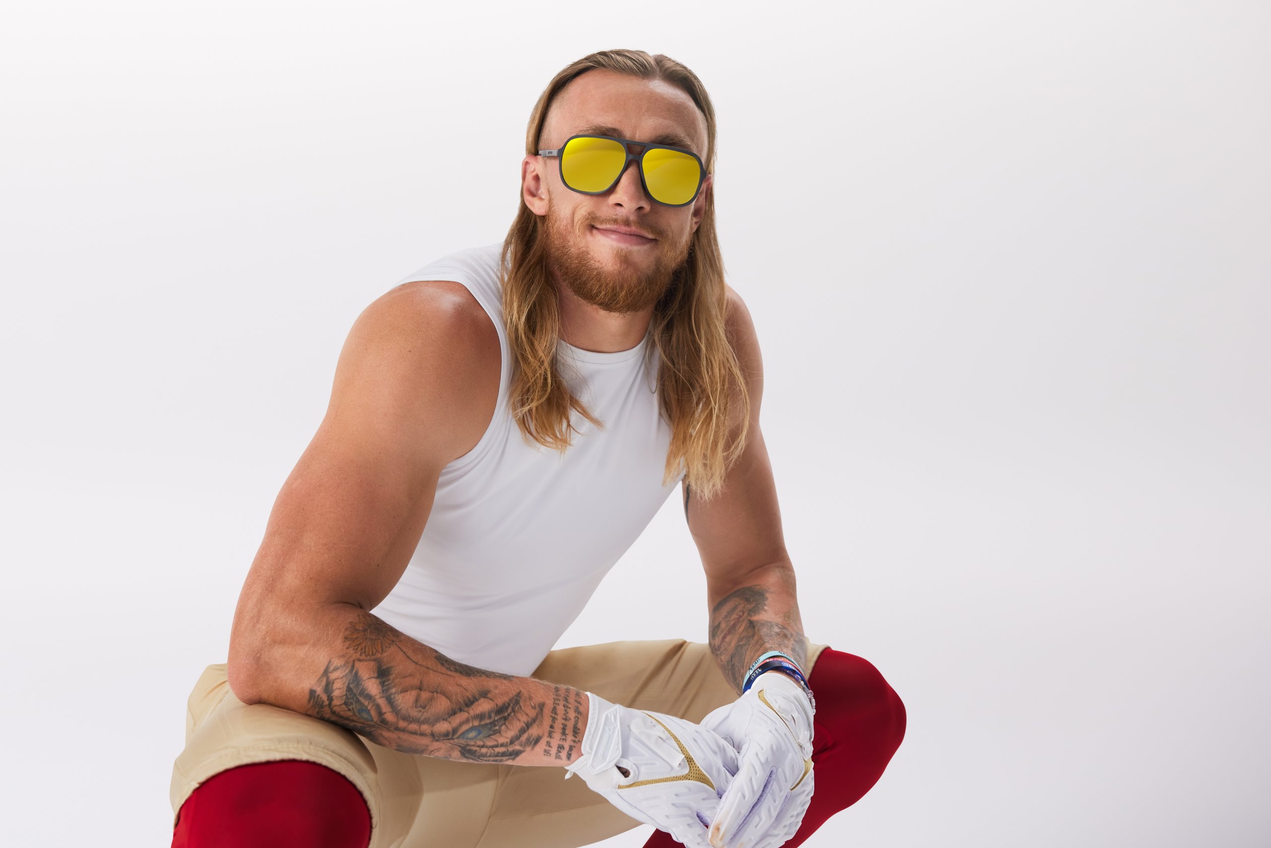 Man wearing reflective yellow sunglasses, white sleeveless shirt, white gloves, beige pants, and red leggings.