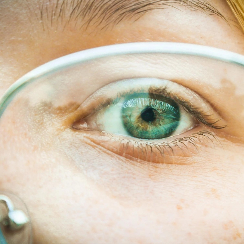 Close-up of a green eye wearing clear glasses.