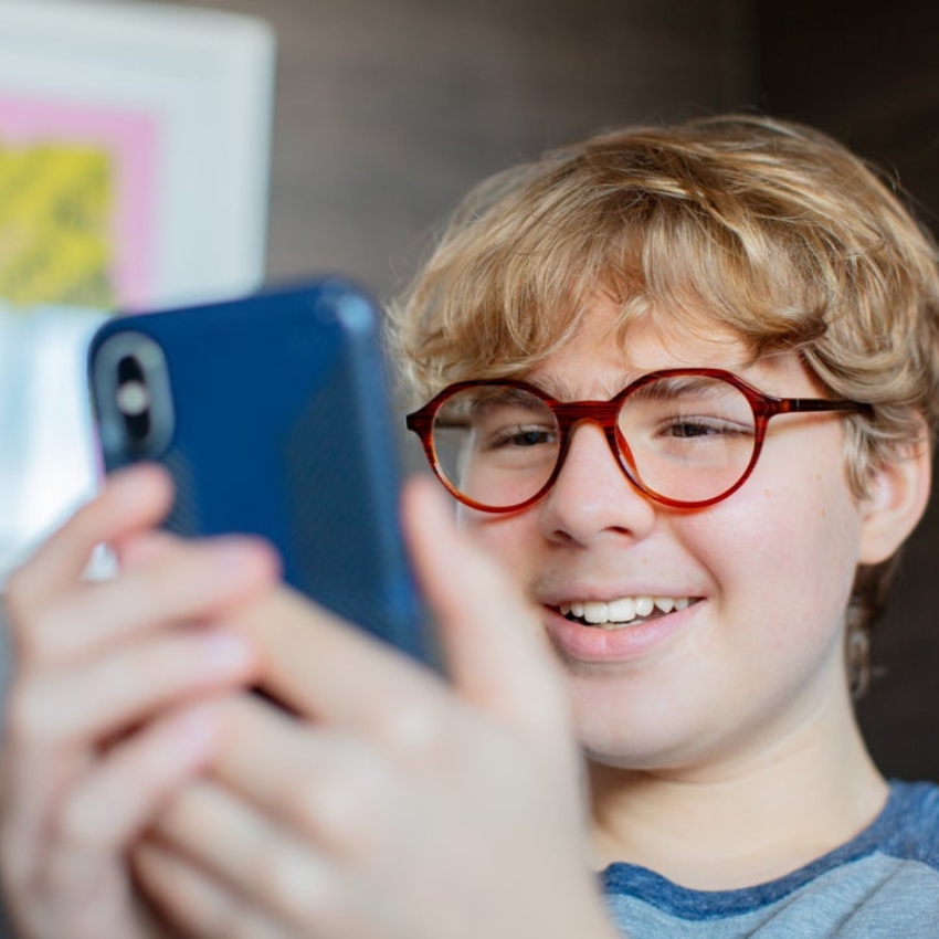 Smiling person wearing glasses holding a blue smartphone.