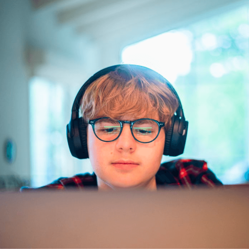 Teen wearing headphones and glasses looking at a screen.