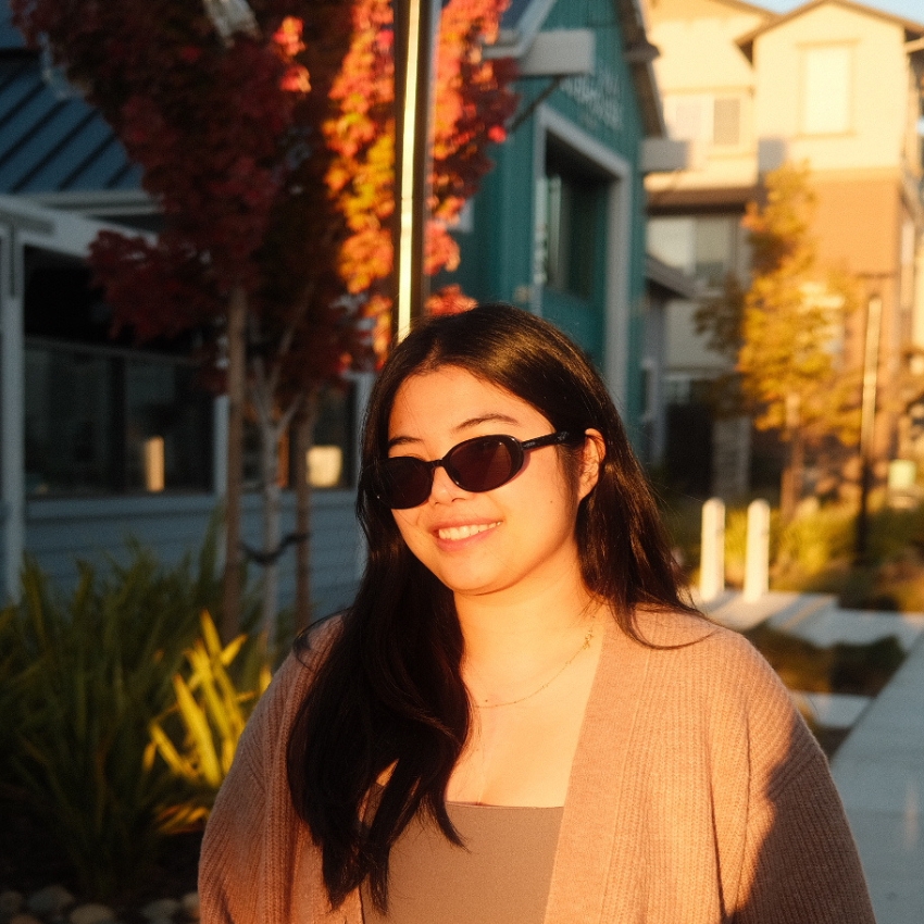 Woman wearing black sunglasses and a beige cardigan, smiling in an outdoor setting.
