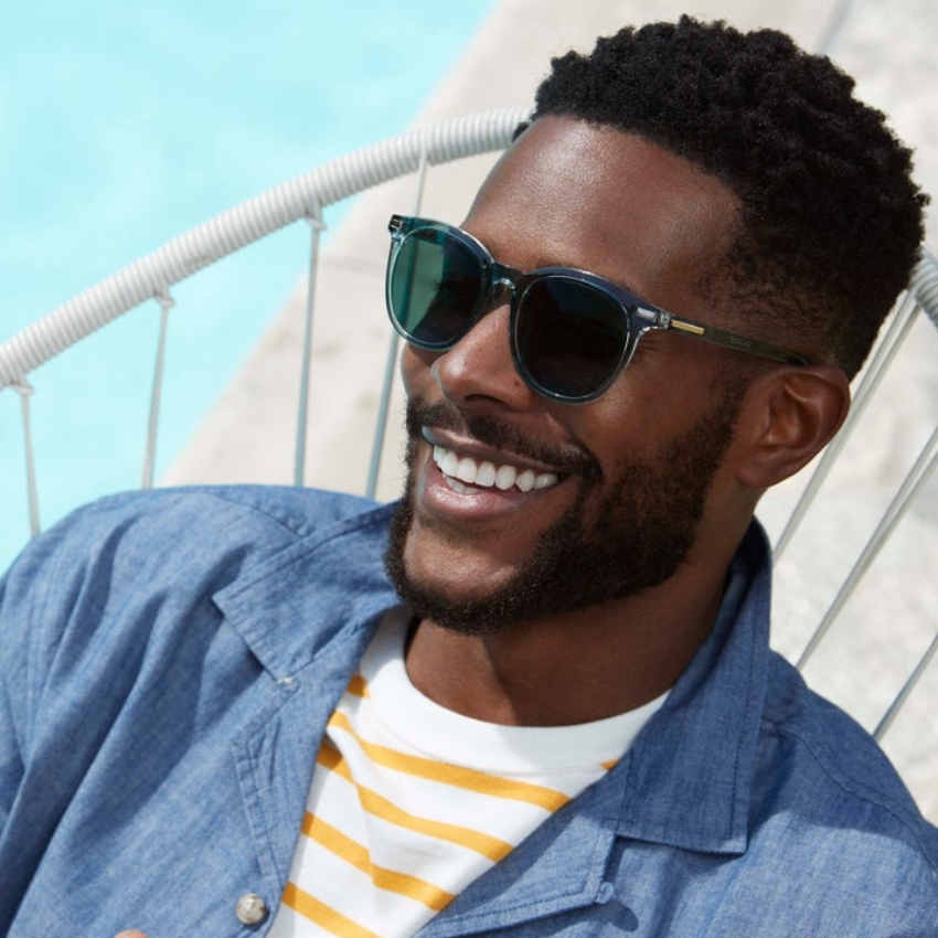 Man wearing stylish black sunglasses and a blue denim shirt over a yellow and white striped T-shirt.