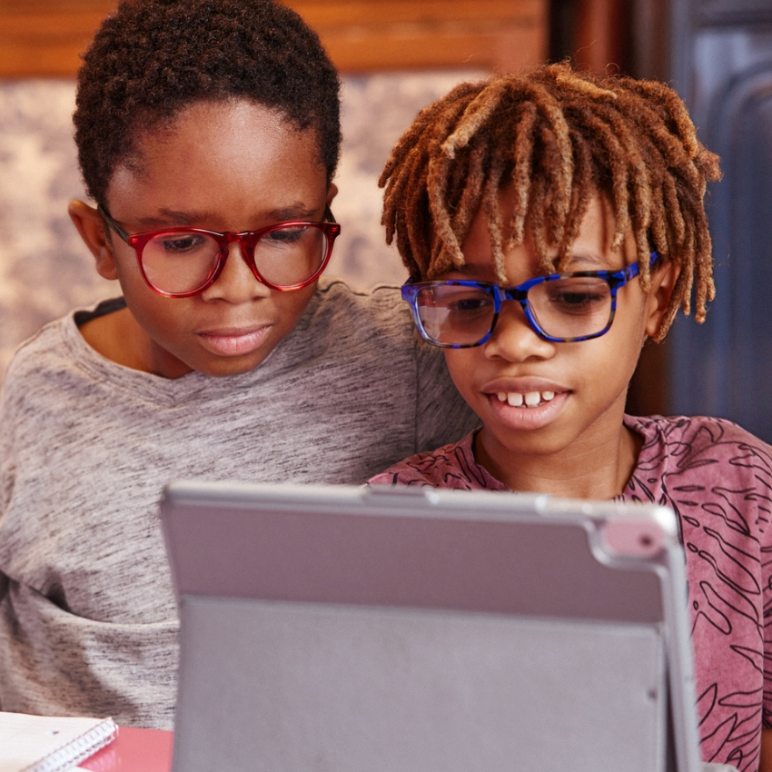 Children wearing colorful glasses, focused on a tablet screen.