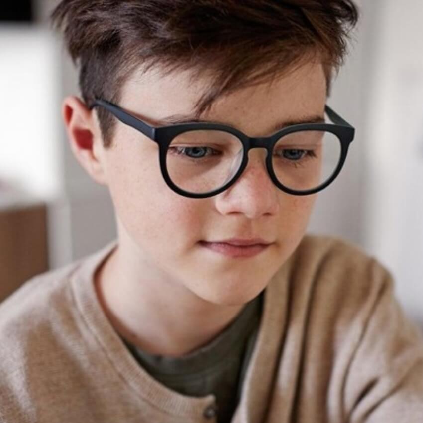 Young person wearing black round eyeglasses and a beige sweater.