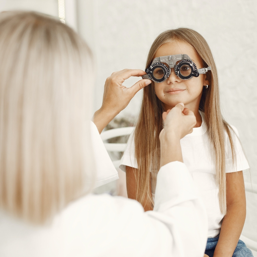 Optometrist adjusting trial frame glasses on a young girl during an eye examination.