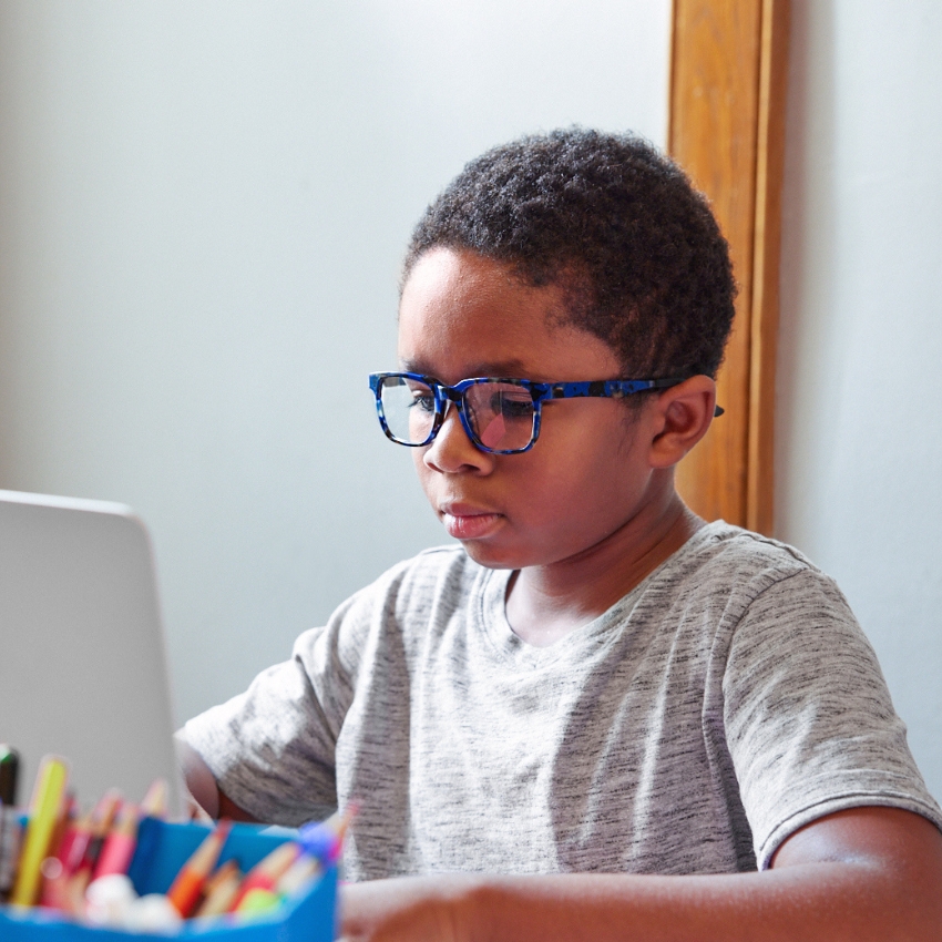 Young boy with blue glasses working on a laptop.