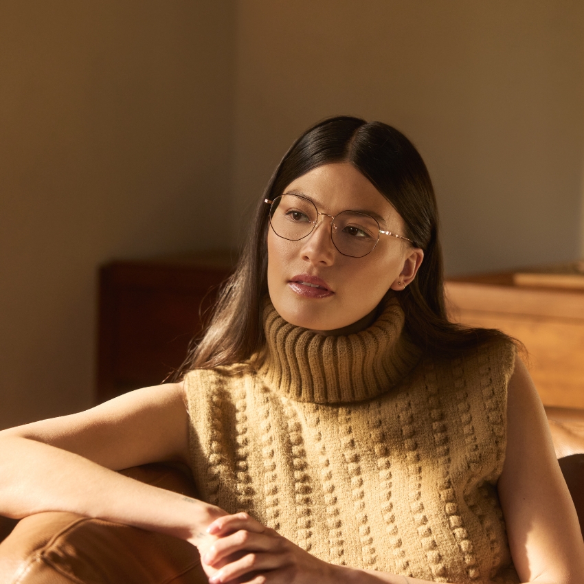 Person wearing silver metal eyeglasses and a sleeveless beige turtleneck sweater.