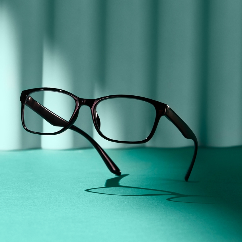 Black eyeglasses with clear lenses on a teal surface.