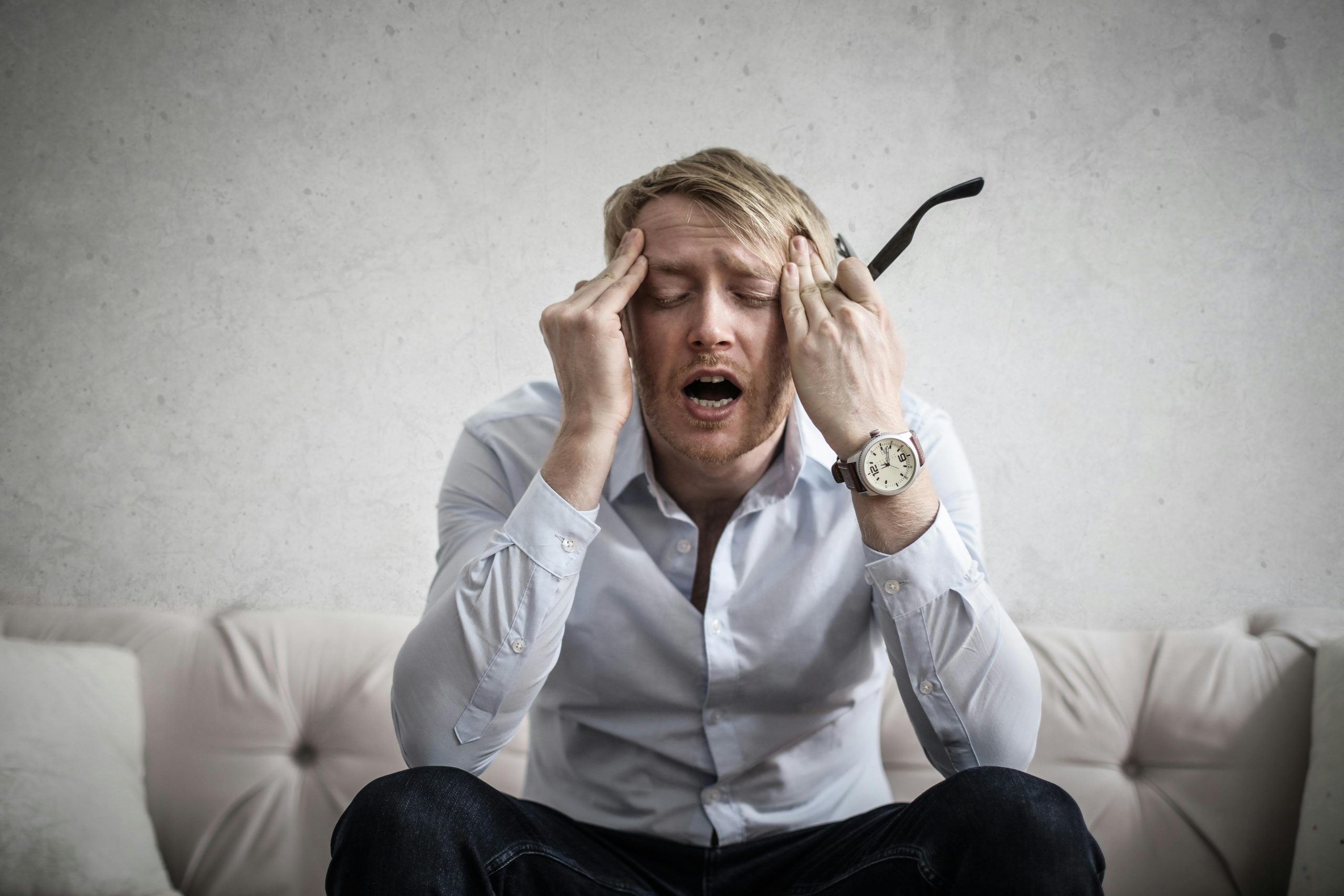 Man in white shirt wearing a wristwatch with a leather strap, appearing stressed with hands on his temples.
