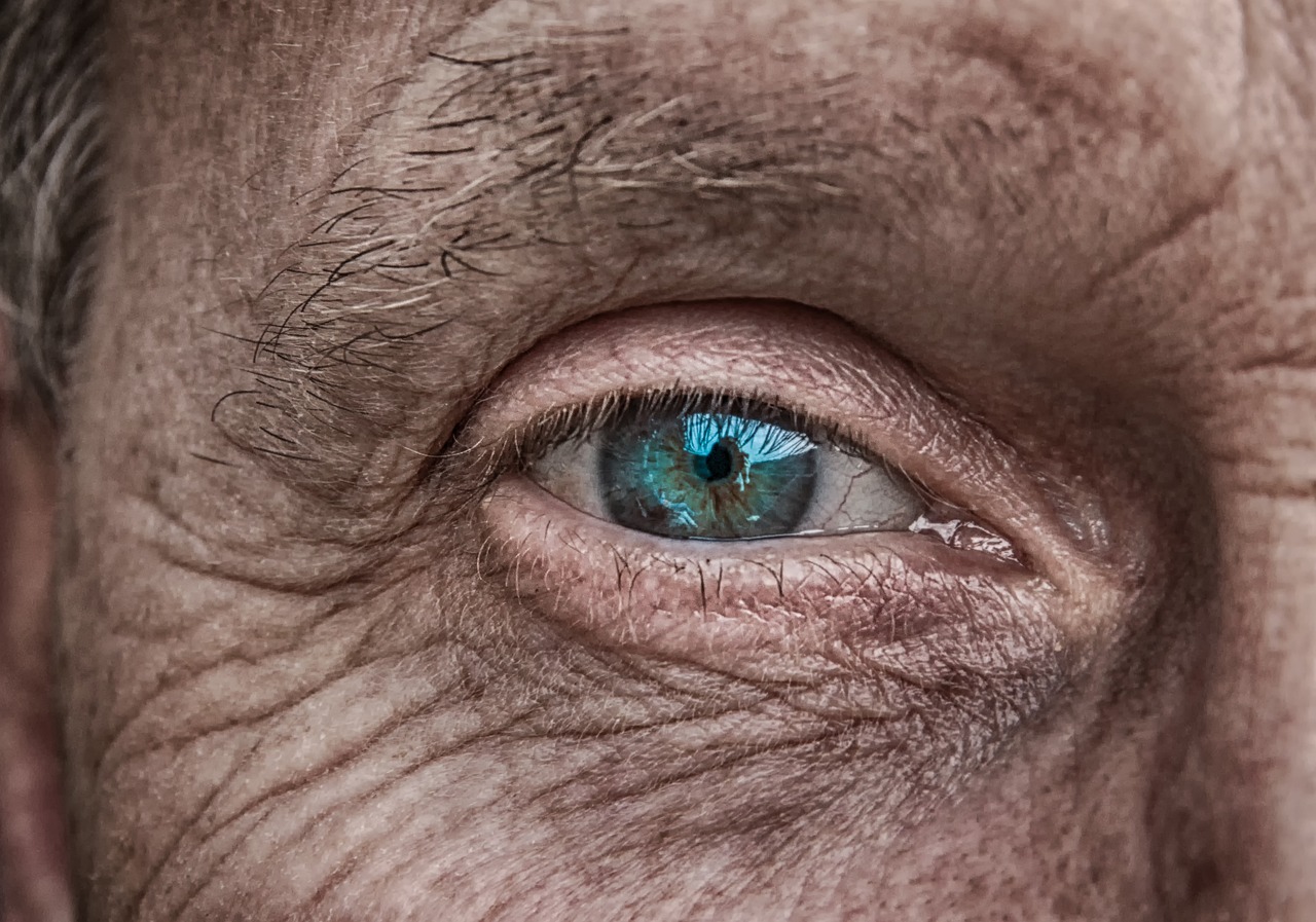 Close-up of an elderly person's eye with a bright teal iris, surrounded by wrinkles and aged skin.