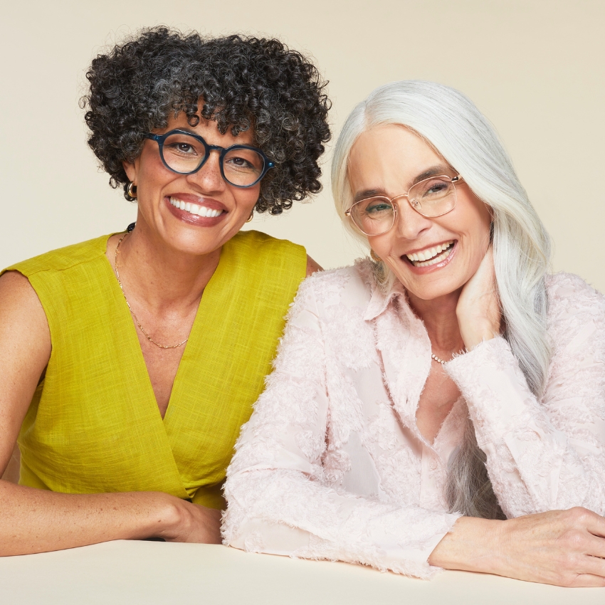 Two women smiling and wearing eyeglasses. One wears a yellow top; the other wears a pink blouse.