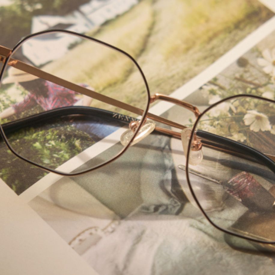 Thin, round-framed eyeglasses with black rims and gold temples resting on a collage of printed photos.