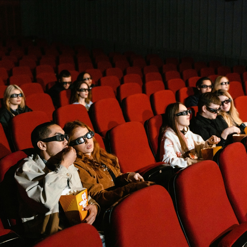 People wearing 3D glasses seated in a movie theater, some holding popcorn containers.