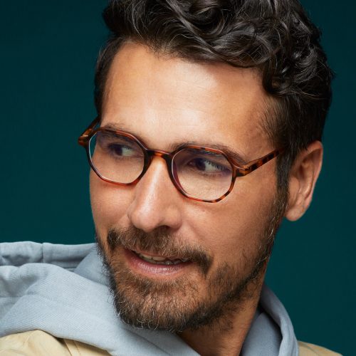 Man wearing tortoiseshell round eyeglasses looking to his left.