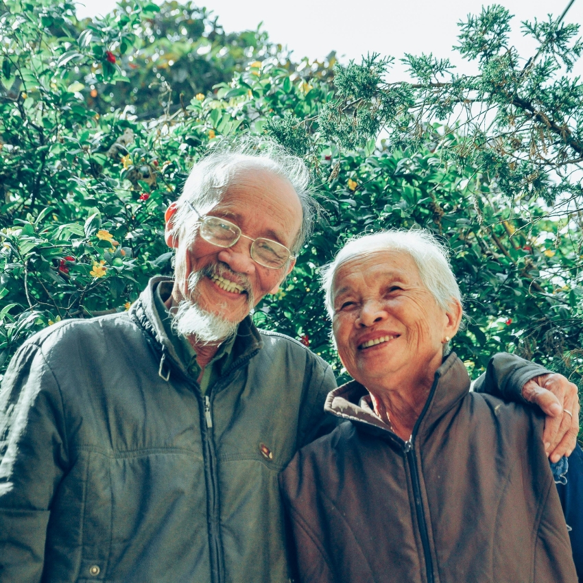 Elderly couple smiling while posing together in outdoor setting.